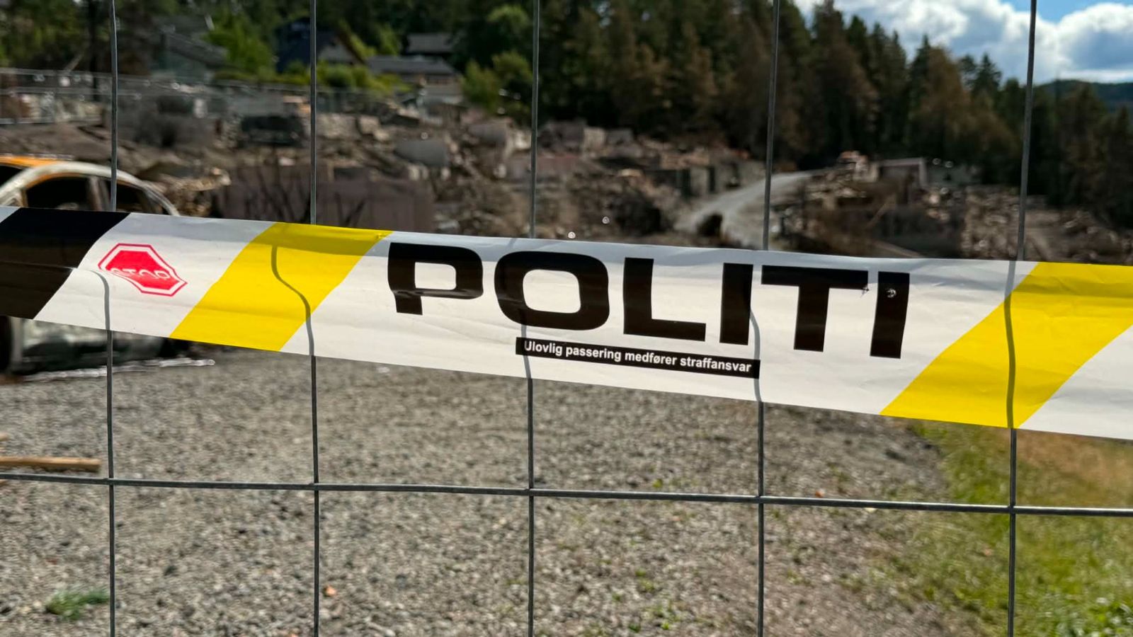 Politisperring ved et brannområde, der utbrente hus og en bilvrak vitner om omfattende ødeleggelser.