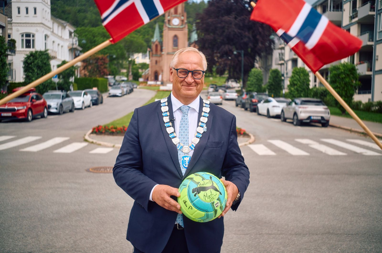 Ordfører Kjell Arne Hermansen med ordførerkjedet og en signert fotball i gatene i Drammen, foran Bragernes kirke.