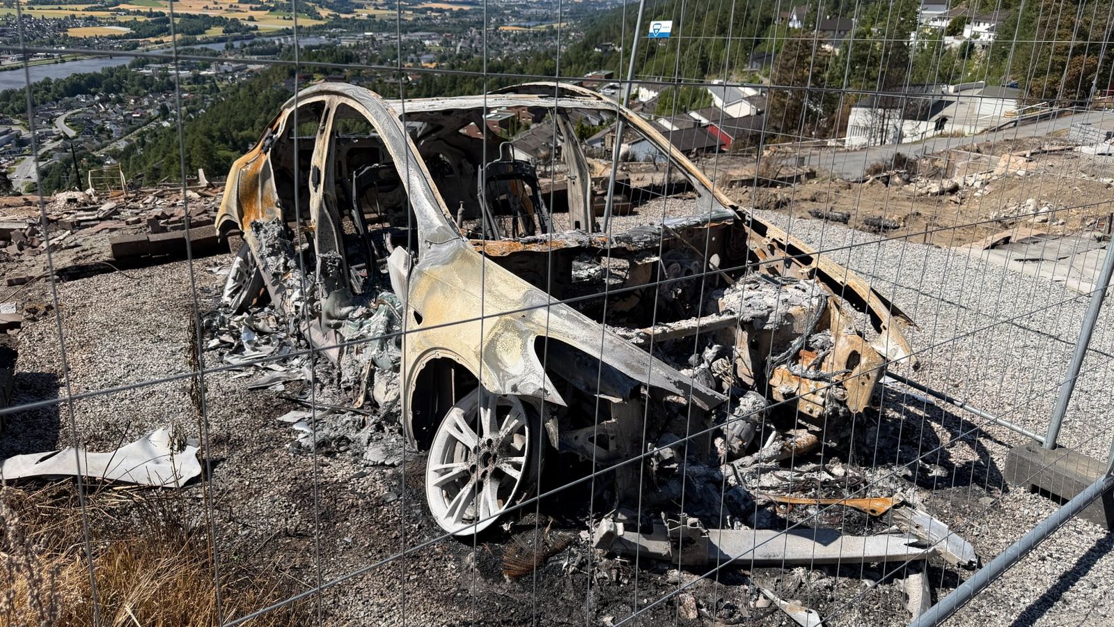 Et utbrent bilvrak står igjen bak sikringsgjerdet på Stenseth, der storbrannen la boliger og eiendeler i aske.