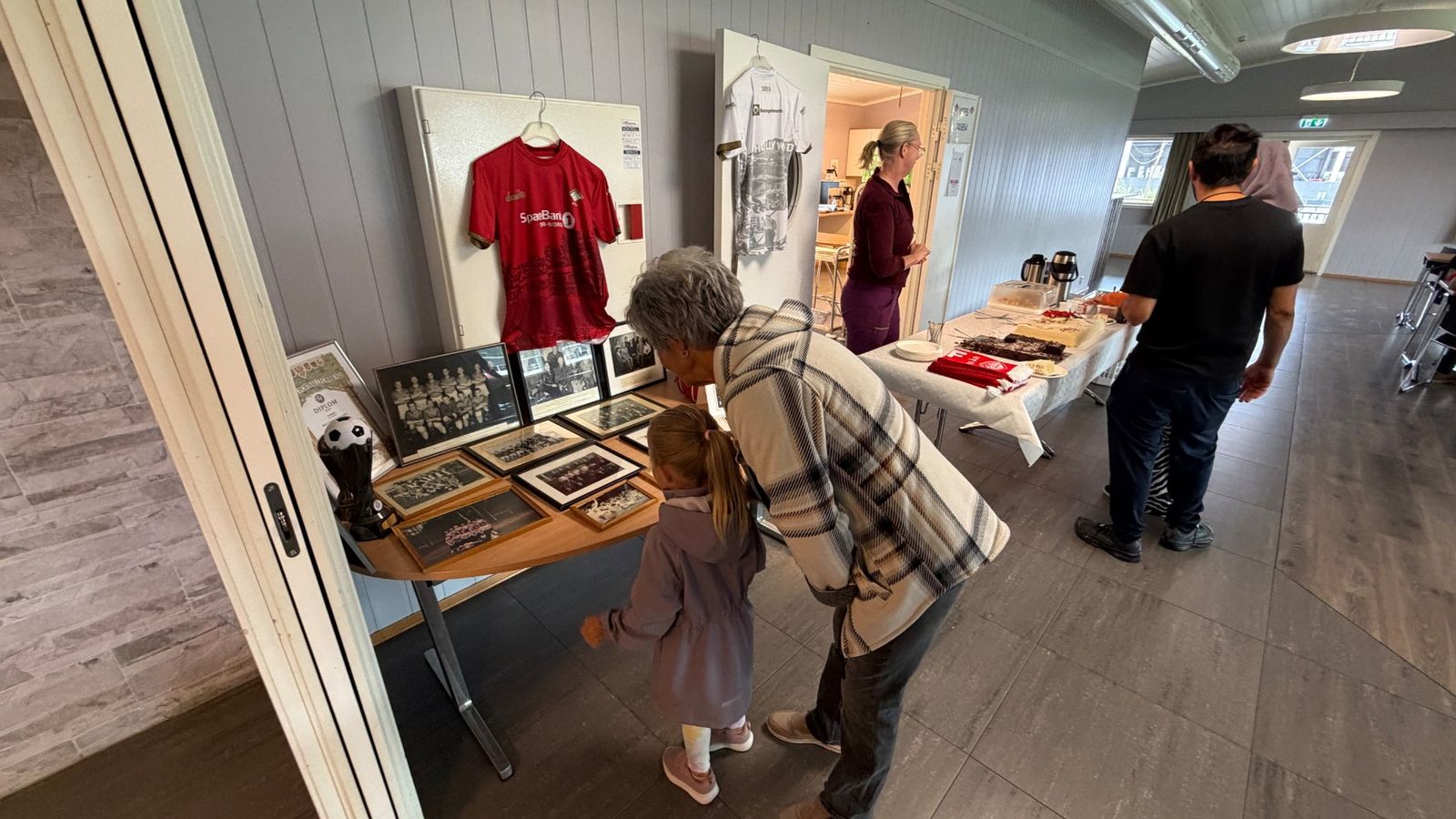 Besøkende studerer klubbens historie gjennom gamle drakter, bilder og pokaler i klubbhuset, mens andre gjør klar kaker og servering til jubileumsfeiringen.