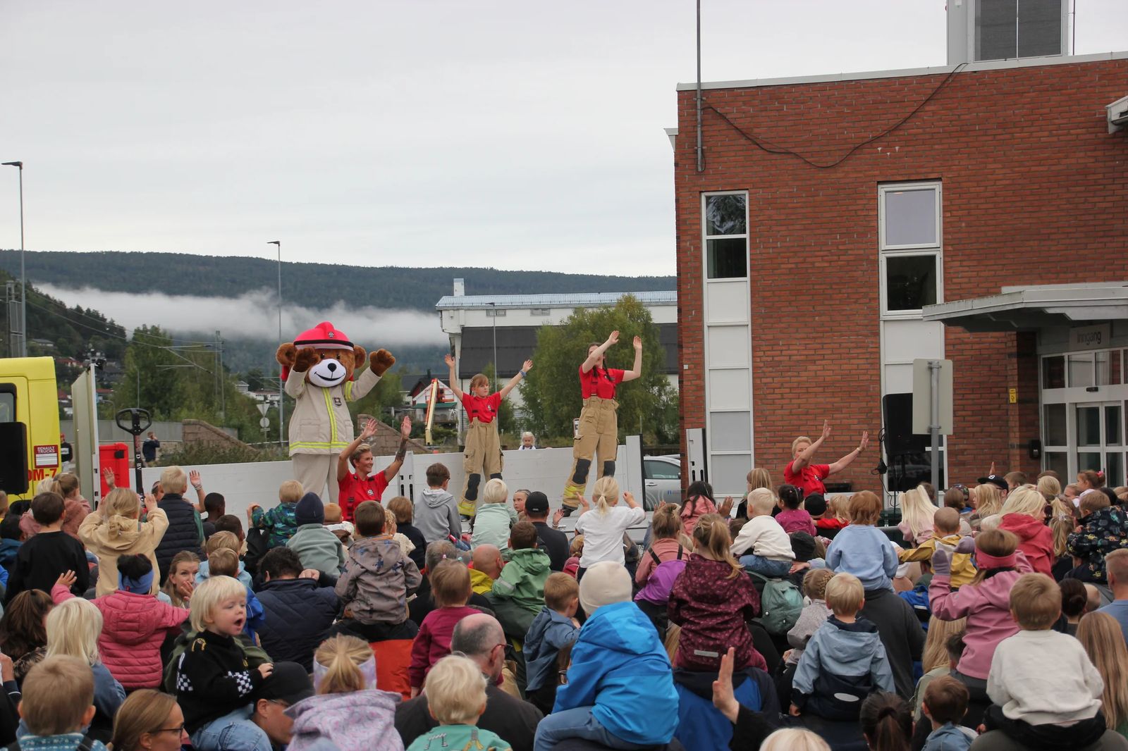 Bjørnis danser sammen med brannvesenets ansatte foran en stor barneflokk under åpen dag ved en av brannstasjonene.