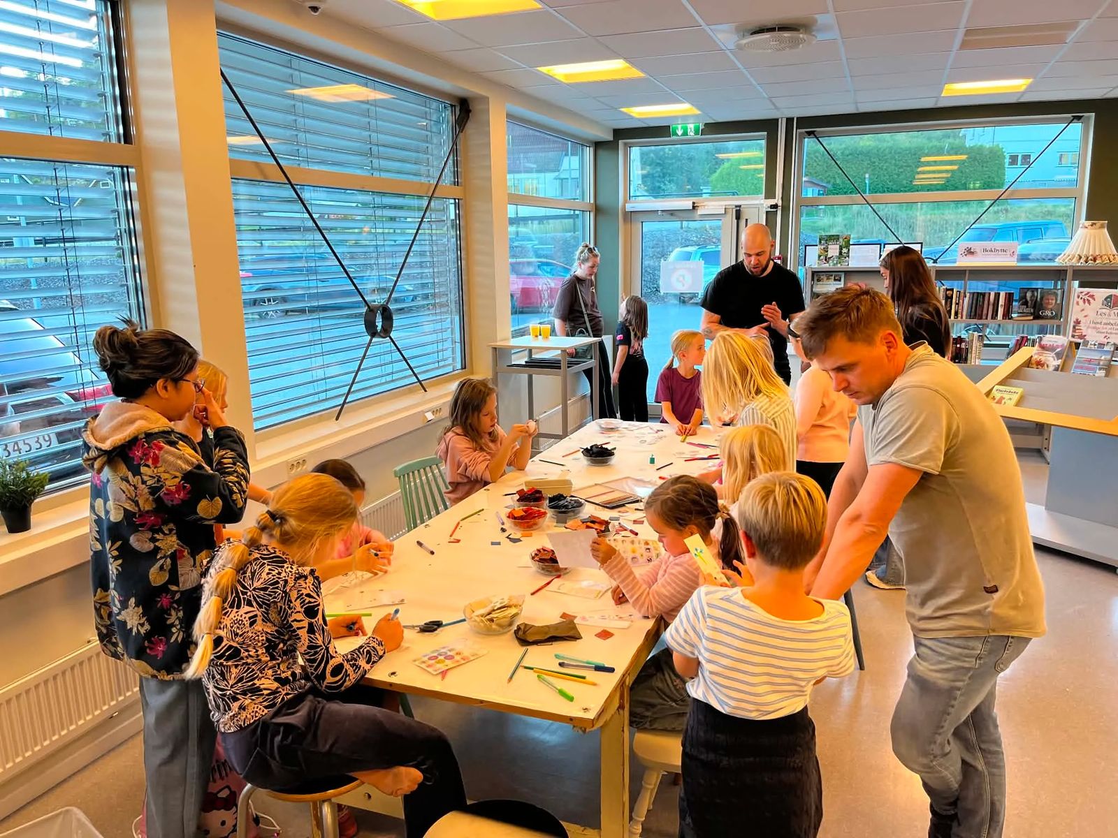 Barn og voksne samlet rundt bordet med tegning og pyssel under åpningsdagen for «Les & Møt» i Skotselv.