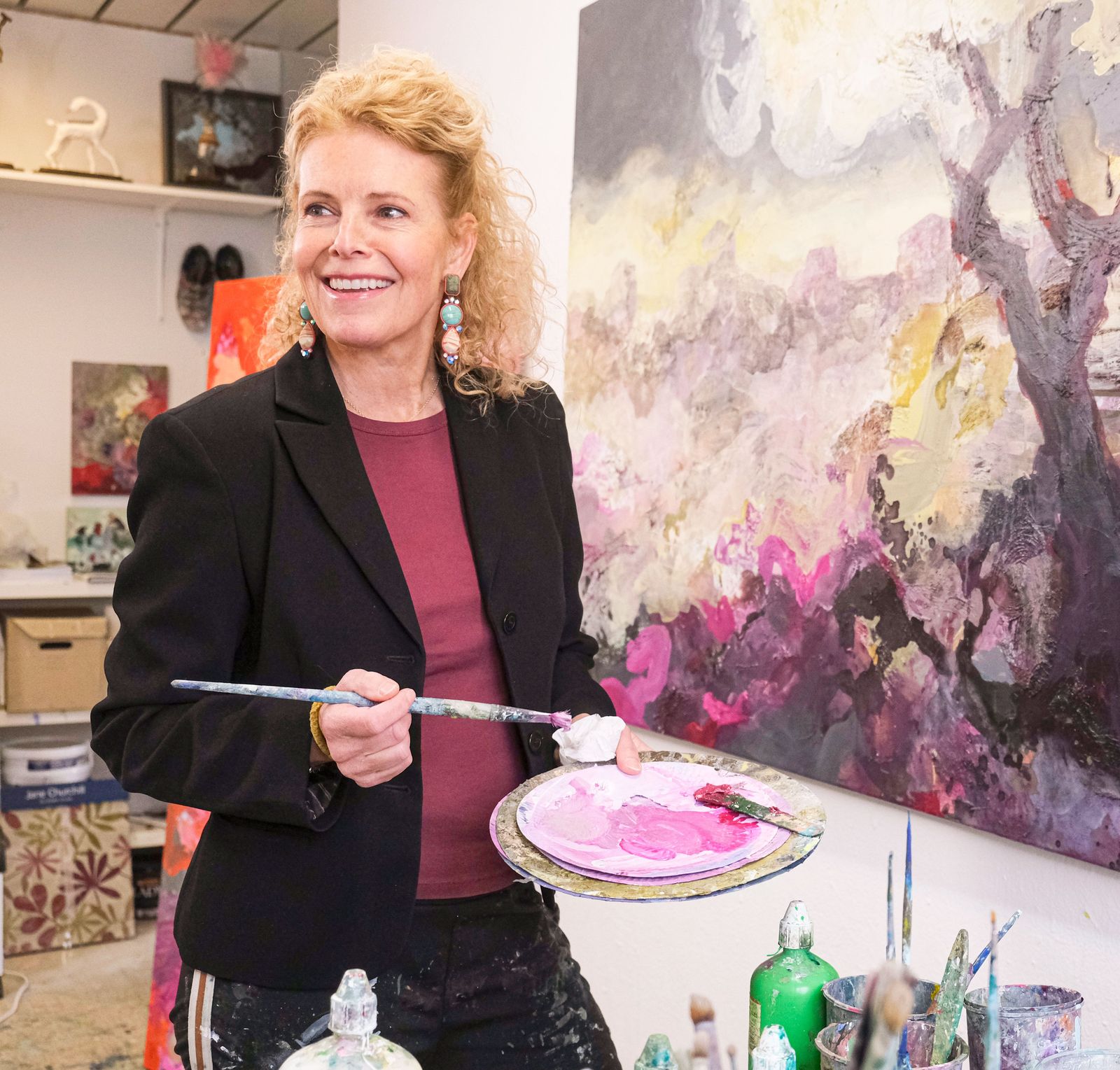 Henriette Finne i atelieret med palett og pensel foran et av sine flammende malerier, i forkant av utstillingen APPASSIONATO på Gulden Kunstverk.